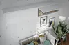 A nursery room with a white wall featuring a hanging cabinet above a crib. The cabinet has one open door revealing some stuffed animals and a basket. There are framed pictures on the wall and a large potted plant next to the crib. Produktbild-Vorschau