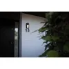 An outdoor wall light fixture is mounted on a white brick wall next to a dark door. The number '15' is visible below the light. Lush green foliage partially obscures the right side of the image. Anteprima dell’immagine prodotto
