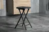 A black folding stool is shown in a room with tiled flooring and wooden cabinets in the background. Anteprima dell’immagine prodotto