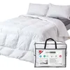 A white goose feather and down duvet is shown laid out on a bed, with two pillows behind it. A white storage bag with the product's branding is in the foreground. Produktbild-Vorschau