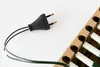 A black electrical plug with green wires is shown on a white background, next to a cardboard holder containing white candle-shaped lights. Produktbild-Vorschau