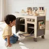 A young boy is playing with a wooden toy kitchen in a room. Podgląd zdjęcia produktu