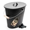 A black oval ash bucket with a lid and handle, placed on a white background with a few pieces of coal next to it. Produktbild-Vorschau