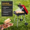 A red and black charcoal grill with food cooking on it, set up on a grassy lawn. Produktbild-Vorschau