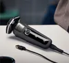 A black electric shaver with a USB charging cable plugged in, resting on a white surface. Náhled obrázku produktu