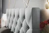 A close-up view of a tufted headboard of a bed, with a wall and a lamp in the background. Produktbild-Vorschau