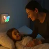 A mother tucks her daughter into bed, illuminated by a butterfly-shaped night light. Produktbild-Vorschau