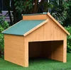 A wooden dog house with a green roof sits on artificial grass, with trees and foliage in the background. Voir les images du produit