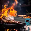 A hand holding a leaf blower aimed at steaks on a grill with flames. Voir les images du produit
