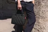 A person holding a black quilted handbag. Voir les images du produit