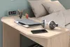 A desk with a laptop, headphones, and a smartphone, next to a bed with pillows. Produktbild-Vorschau