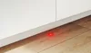 A close-up view of a red LED light on a wooden floor near a white cabinet baseboard. Produktbild-Vorschau