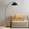 A black arc floor lamp is positioned next to a beige sofa with a yellow pillow and a green throw blanket. Produktbild-Vorschau