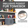 A display of shelves with various figurines and a gray Toniebox, with a close-up inset showing a wooden stand with a circular cutout. Produktbild-Vorschau