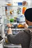 A person is reaching into a refrigerator filled with food items. Produktbild-Vorschau