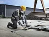 A construction worker is kneeling and using an angle grinder to cut metal in an outdoor industrial setting. Náhľad obrázku produktu