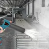 A hand holding a blue and black leaf blower in a factory setting, blowing white dust or debris. Voir les images du produit