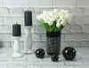 A still life arrangement of decorative items including black candles on white candle holders, a vase of white tulips, and black decorative spheres. Anteprima dell’immagine prodotto