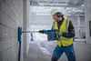 A construction worker is using a hammer drill to drill into a concrete block wall. Produktbild-Vorschau
