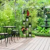 A garden setting with a table and chairs, a plant stand, and a fountain. Náhľad obrázku produktu
