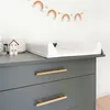 A changing table with a white changing pad on top of a gray dresser, with a rainbow garland hanging on the wall above. Produktbild-Vorschau