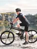 A man is riding an electric bicycle near a body of water with rocky hills in the background. Produktbild-Vorschau
