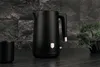 A black electric kettle with rose gold accents is displayed on a dark countertop, with a small black cup and a potted plant in the background. Náhľad obrázku produktu