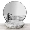 A marble-patterned sink with a black faucet is placed on a wooden surface in front of a large circular mirror. Náhled obrázku produktu