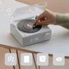 A hand is shown adjusting a knob on a white retro-style Bluetooth speaker that resembles a record player. Musical notes are depicted floating around the device, suggesting music playback. The device has a digital display showing '10:06'. Below the device,  Podgląd zdjęcia produktu