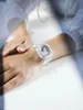 A person's wrist wearing a transparent watch, with soft lighting and shadows. Voir les images du produit