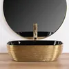 A gold and black basin with a gold faucet is shown in front of a round mirror. Anteprima dell’immagine prodotto