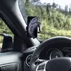A smartphone mounted on a car windshield mount, with the steering wheel and dashboard visible in the foreground and a forest scene in the background. Produktbild-Vorschau