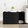A black wooden cabinet with two doors and an open compartment, placed next to a sofa. A lamp, books, and a cup of coffee are on top of the cabinet. Produktbild-Vorschau