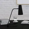 A black desk lamp is positioned on a black desk in front of a white brick wall. Next to the lamp are a stack of books and a small coffee maker with a cup. Podgląd zdjęcia produktu