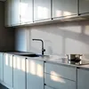 A modern kitchen counter with a sink, faucet, and a pot on a stovetop, with sunlight streaming in. Produktbild-Vorschau