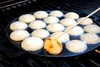 A close-up shot of a cast iron poffertjes pan on a grill, with poffertjes being cooked. Anteprima dell’immagine prodotto