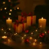 Christmas-themed arrangement with gifts, candles, pine cones, and fairy lights on a wooden surface. Produktbild-Vorschau