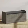 A grey rattan storage bench with a dark grey cushion sits on a wooden deck in front of a light grey wall. Anteprima dell’immagine prodotto