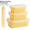 Three stackable yellow silicone food containers with white lids are shown. One container is shown folded flat on the left side of the image. Podgląd zdjęcia produktu