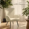 A cream-colored armchair is placed in a well-lit room with plants and sunlight streaming through the window. Produktbild-Vorschau