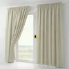 Two cream-colored blackout curtains are shown hanging on a window. One curtain is partially open, revealing a landscape view outside. A small sun icon is overlaid on the right curtain. Produktbild-Vorschau