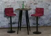 Two red bar stools are placed around a small square bar table with a bottle of wine and two glasses on it, in front of a stone wall. Podgląd zdjęcia produktu