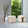 Two beige upholstered stools are placed on a concrete floor next to a window with lush green foliage visible outside. A tall, narrow brown vase and a white textured vase are also present. Produktbild-Vorschau