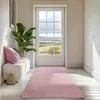 A pink runner rug is laid out on a light wooden floor in a hallway, leading towards a glass-paneled door with a view of a green landscape. A white bench with a pink cushion and a potted plant are visible to the left. Produktbild-Vorschau