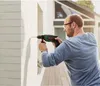 A man is drilling into a white wall outdoors. Produktbild-Vorschau