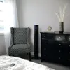 A bedroom scene featuring a tall black fan next to a patterned armchair and a black dresser. Anteprima dell’immagine prodotto