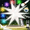 A collection of illuminated star-shaped decorations, some in various colors and one large white one in the center, displayed outdoors on grass with a remote control and power adapter. Produktbild-Vorschau