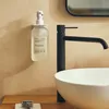 A bathroom sink area with a soap dispenser mounted on the wall next to a black faucet and a white sink. Produktbild-Vorschau