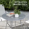 A round bistro table with a plant and books on it, set on a patio with chairs and greenery in the background. Náhled obrázku produktu