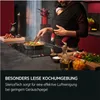 A person is cooking while holding a baby, with food and kitchenware visible. Produktbild-Vorschau